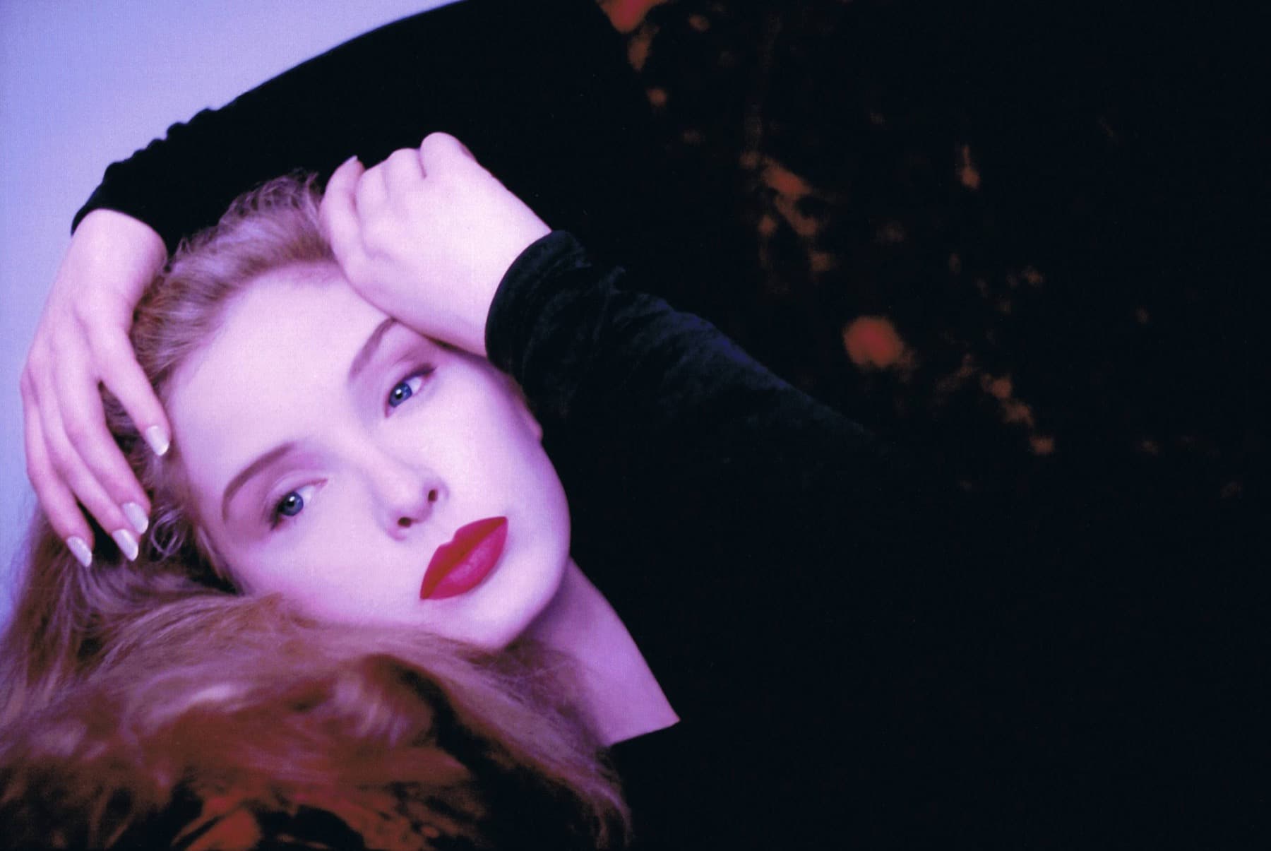 Julie Delpy in 1995, lying back with one hand in her hair, in a dark velvet top