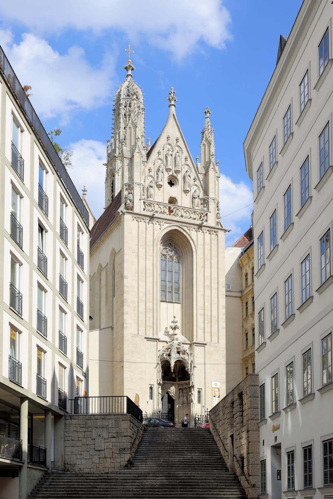 A narrow Gothic church front at the top of a flight of stone steps between plain buildings