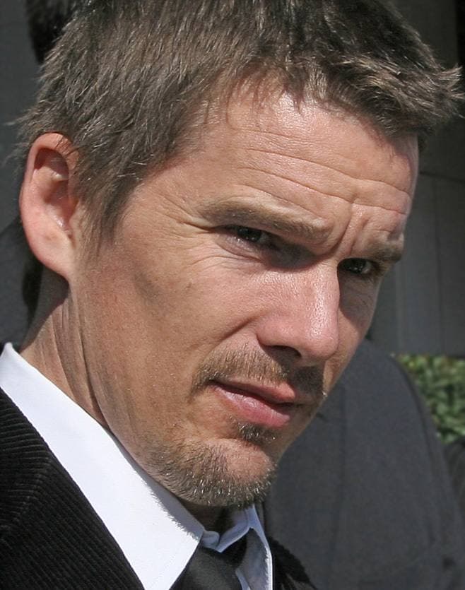 Ethan Hawke, unshaven, in a dark suit and white shirt, looking at the camera