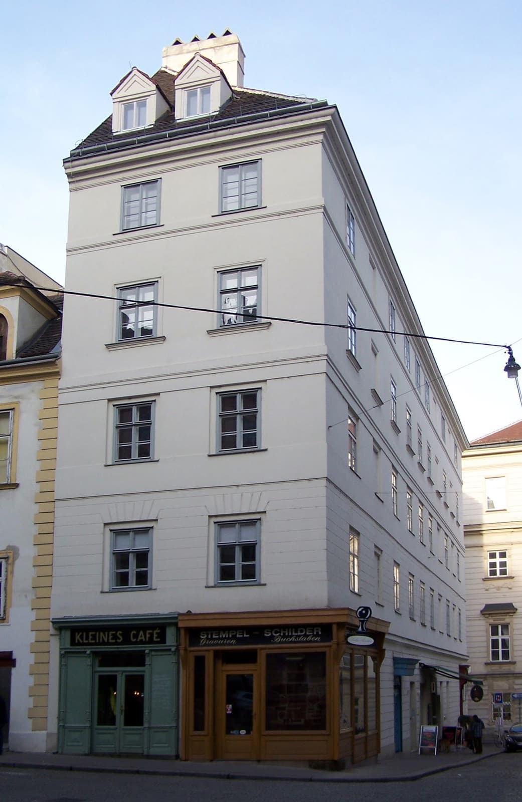 A tall white corner house with a small café shopfront at street level