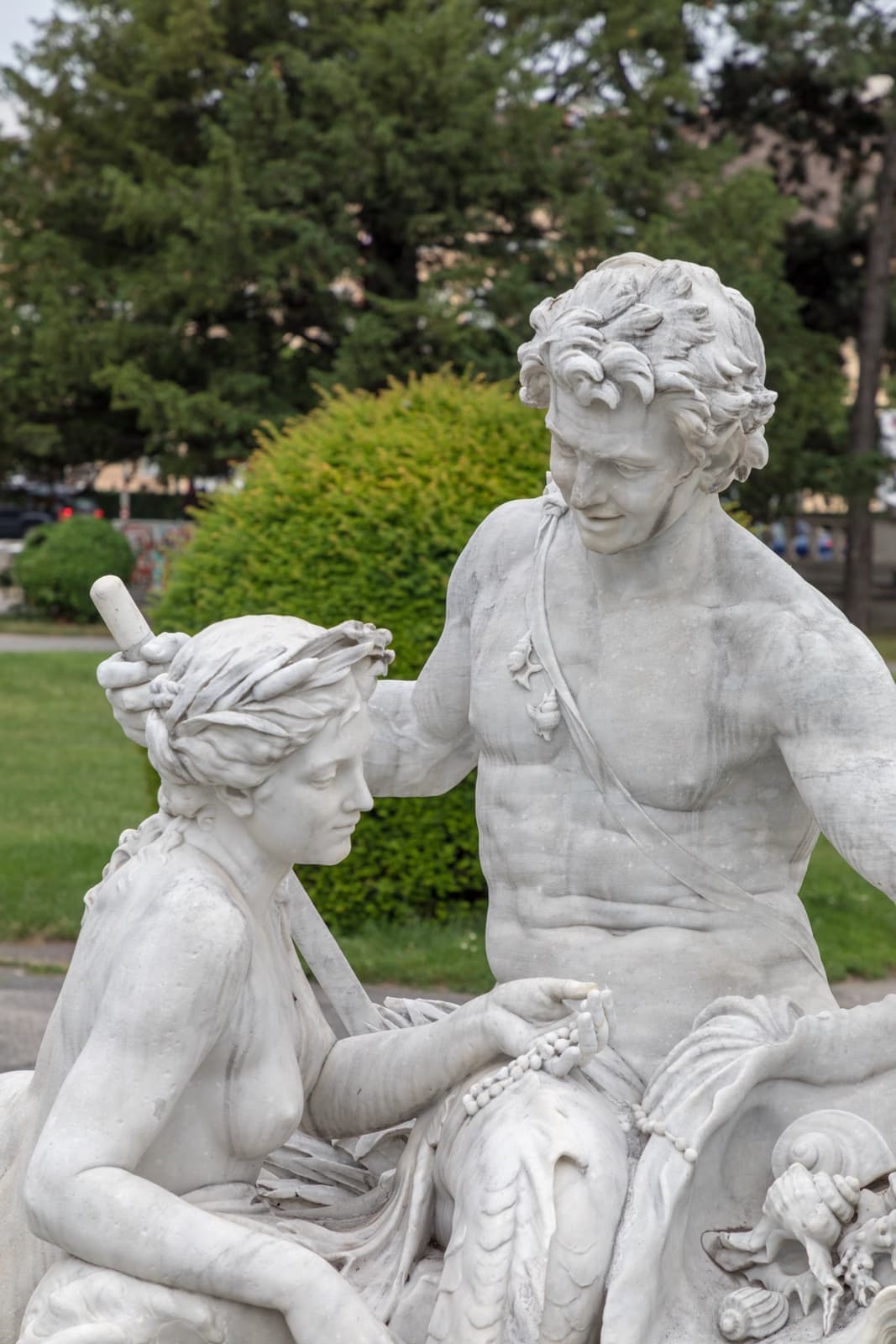 White marble figures of a man and a woman beside a fountain, with greenery behind