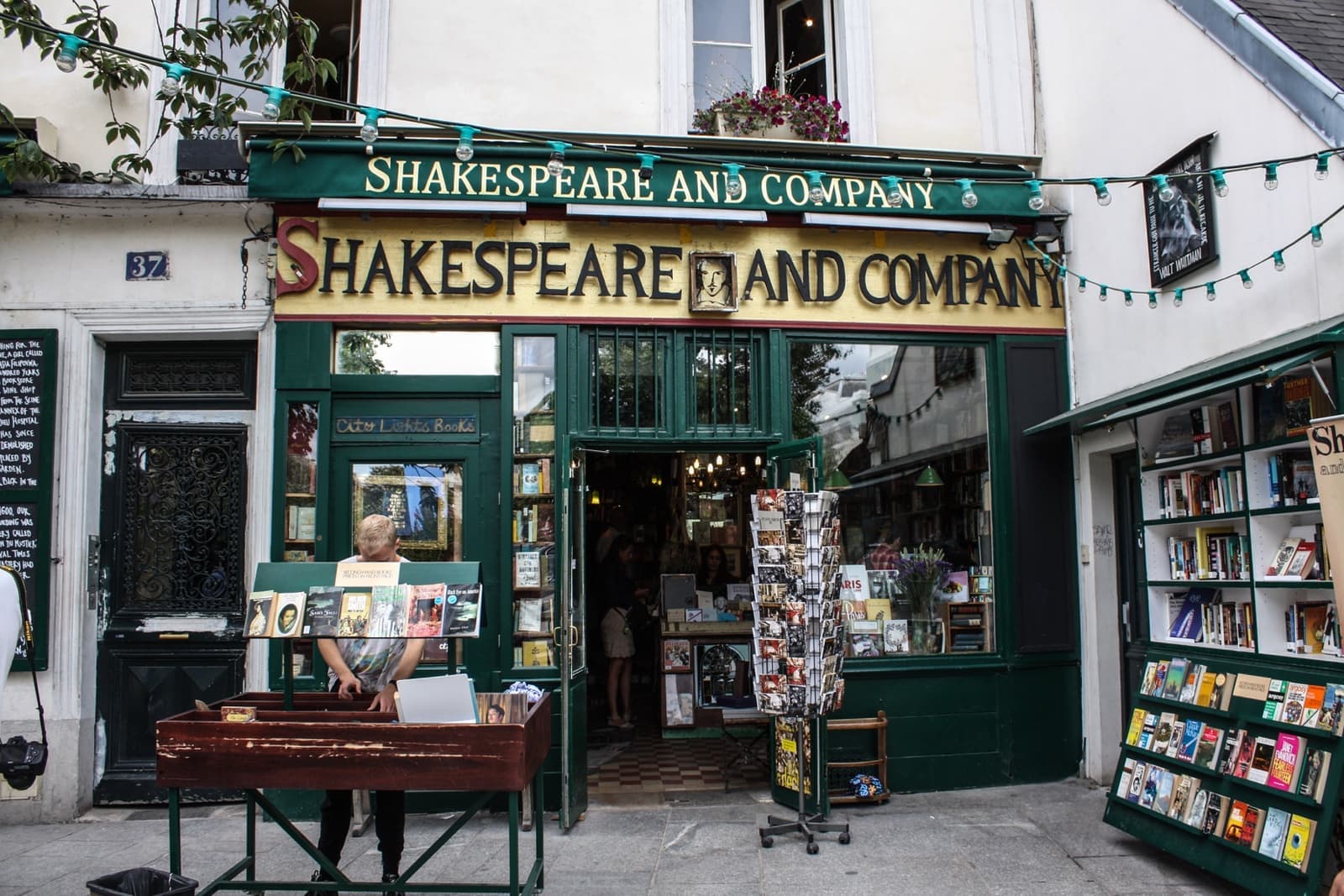 A green-fronted bookshop with its name in yellow letters and book racks outside