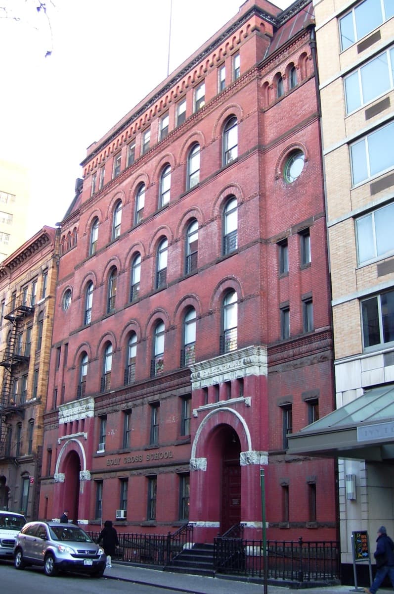 A red brick school building with arched windows on a city street