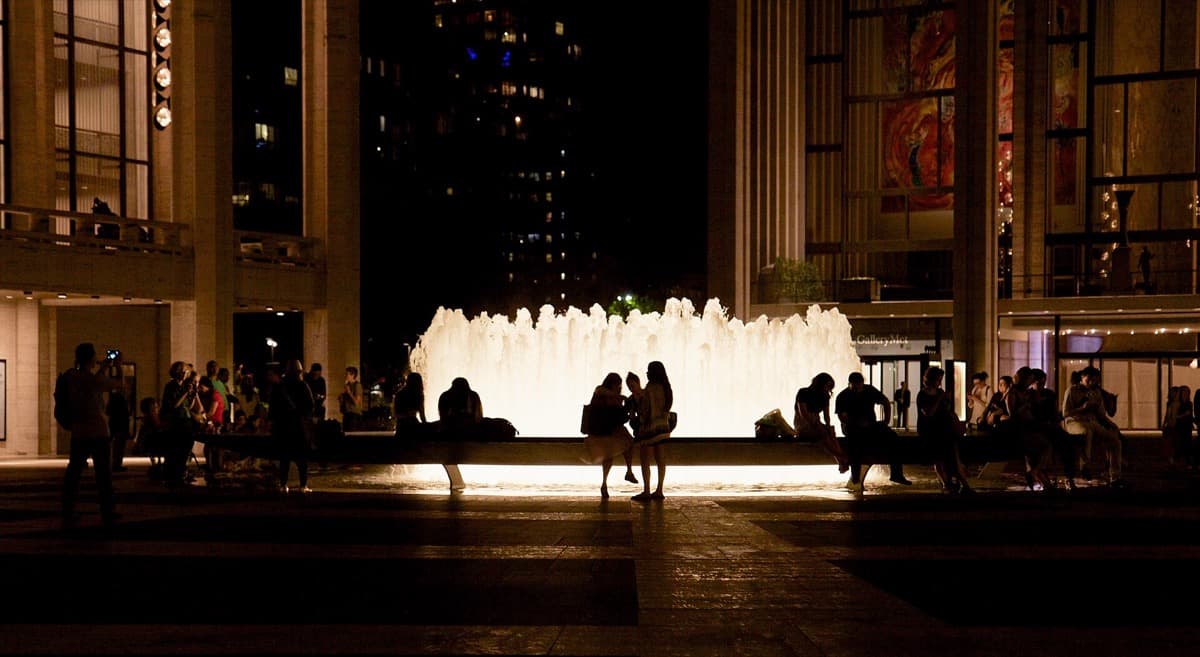 A lit circular fountain on a plaza at dusk