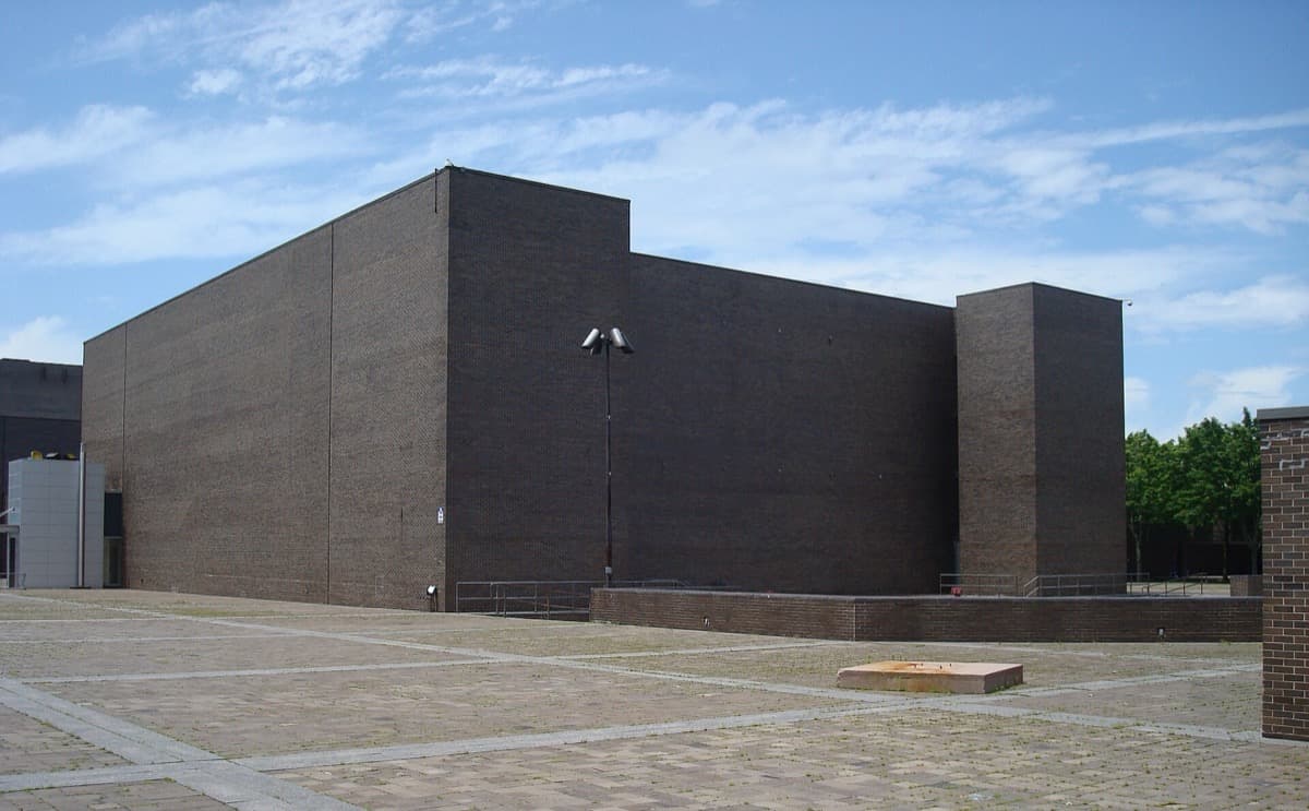 A low concrete arts centre beyond a paved plaza