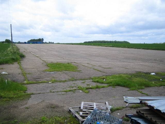 A wide strip of old concrete runway running into the distance between grass