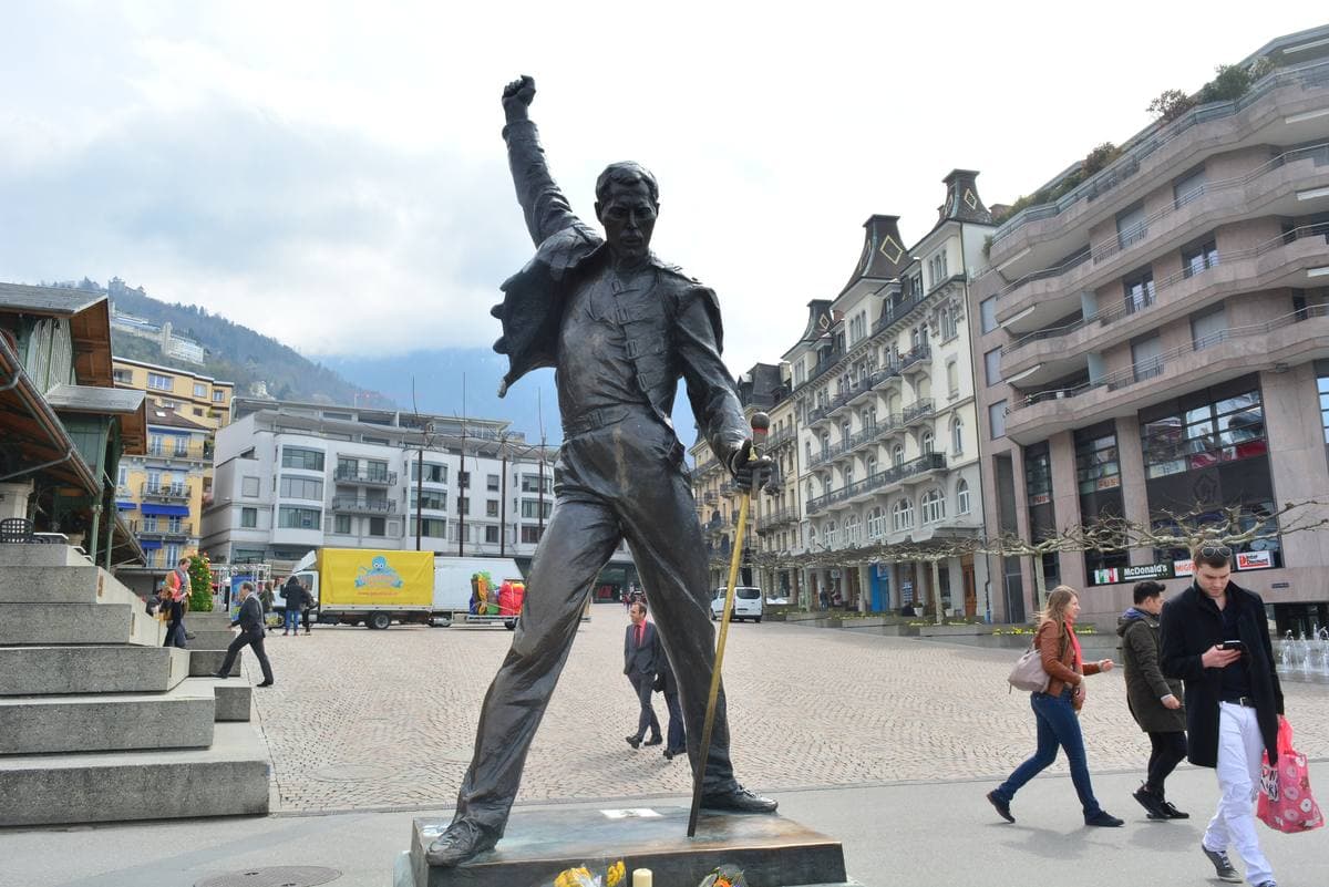 The statue of Freddie Mercury on its plinth beside the lake and mountains