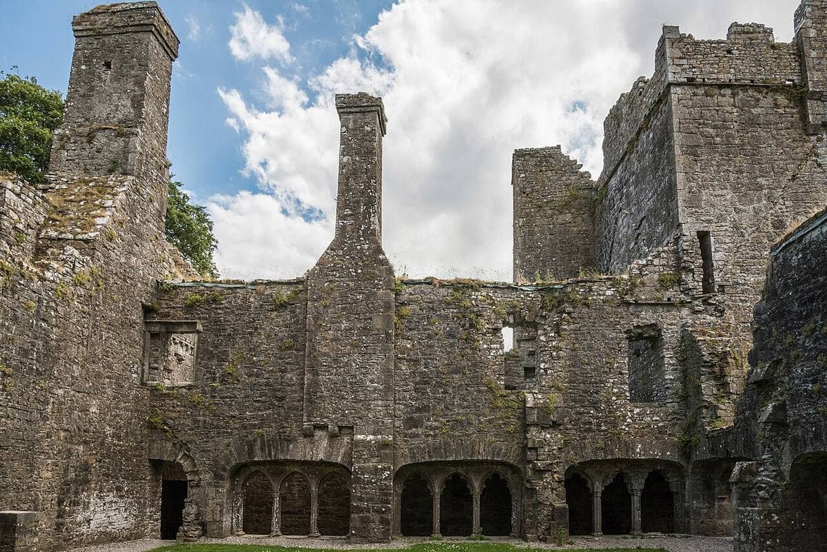 Grey stone ruins with tall chimneys and a row of pointed cloister arches
