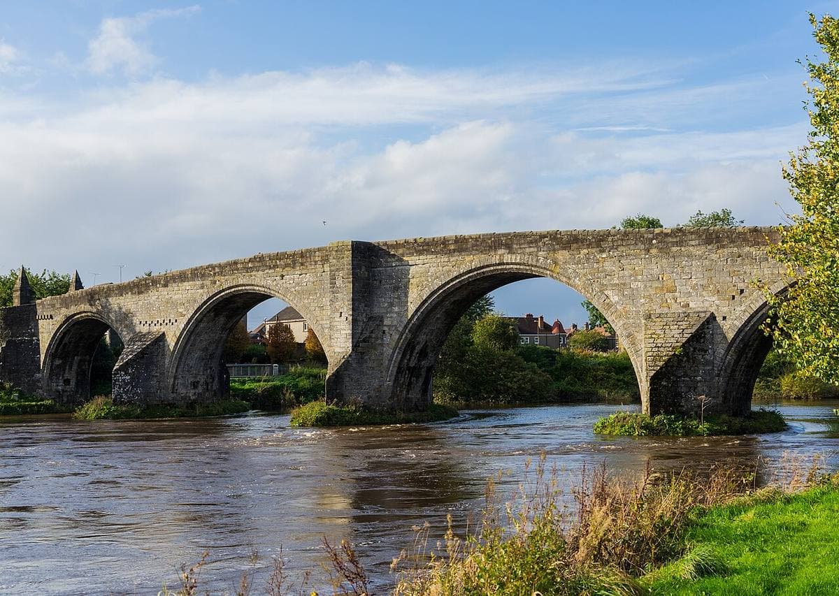 A four-arched stone bridge over a river on a bright day