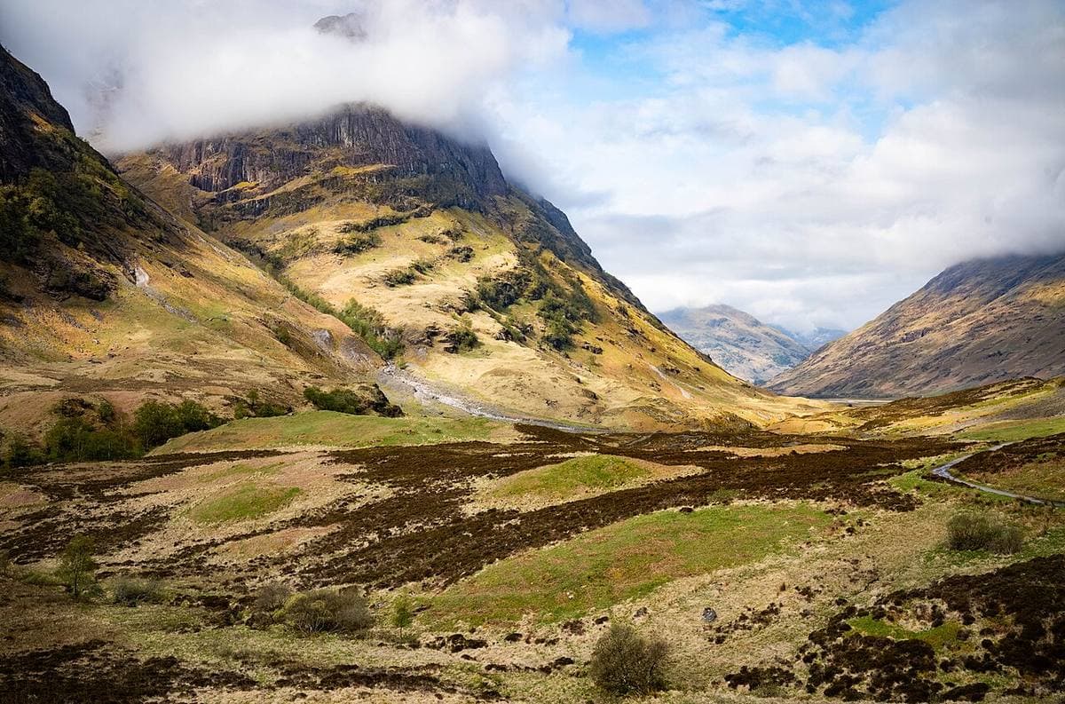 Steep green and brown mountains on either side of a wide glen, cloud on the tops