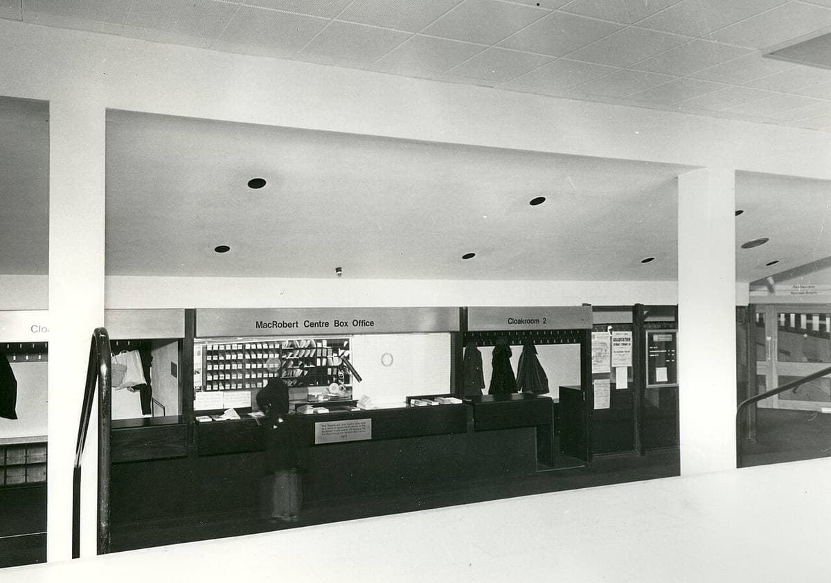 A black-and-white photograph of a modern foyer with a box-office counter