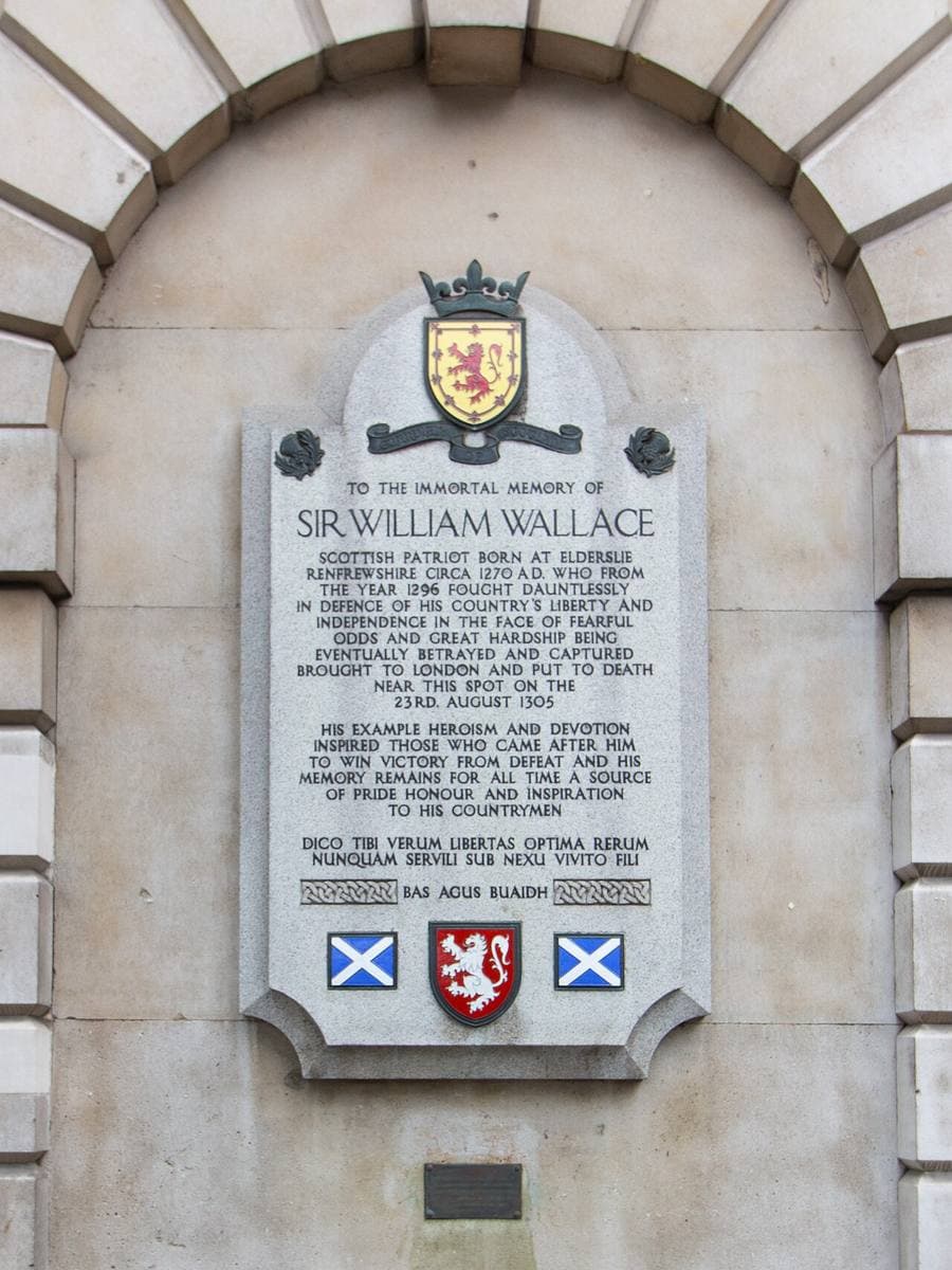 A carved stone tablet with a crest and saltire shields set into a stone wall