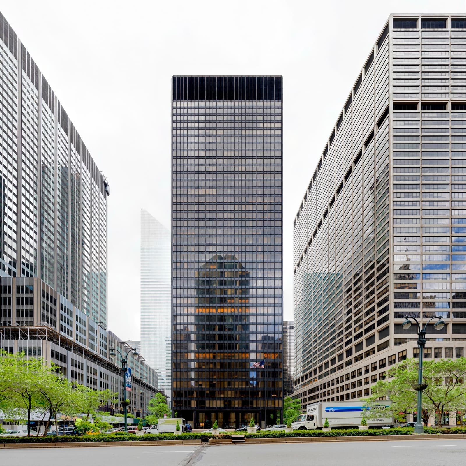 A dark bronze-and-glass tower set back behind an open plaza, between pale office blocks