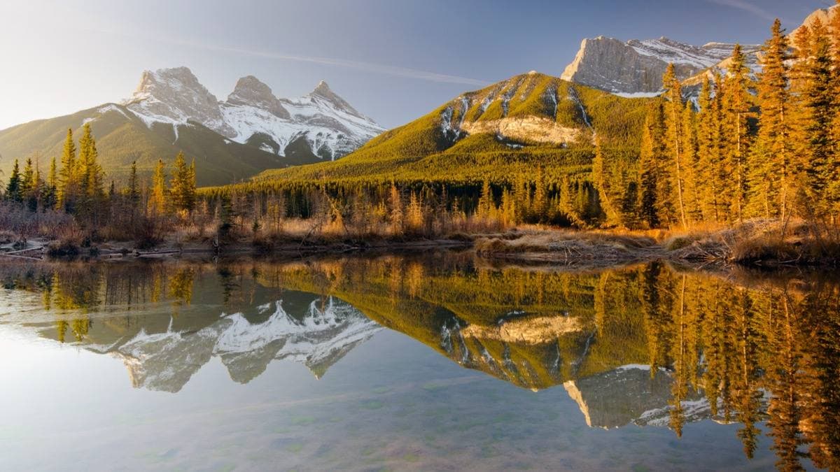 Three snow-streaked peaks above a still creek and spruce