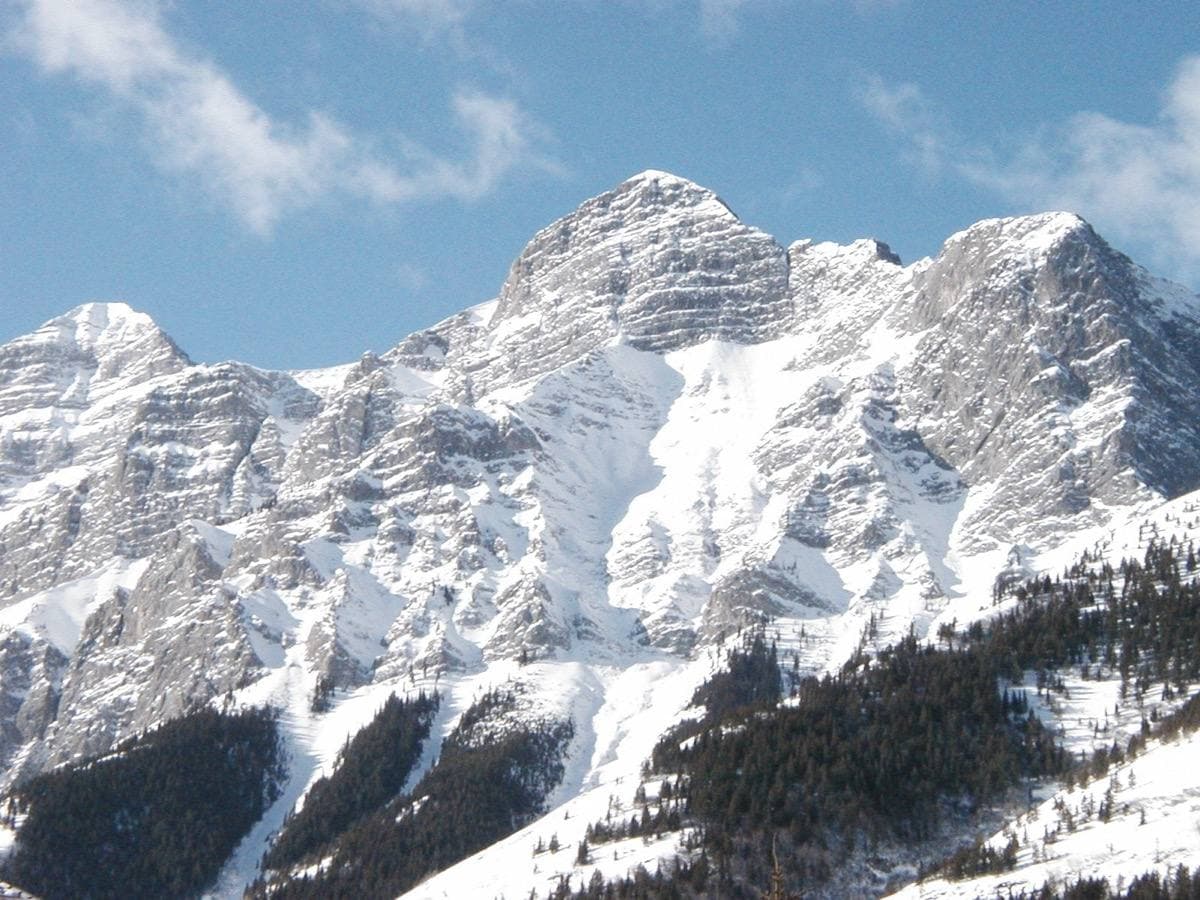 A snowy mountain face across a valley under a pale sky