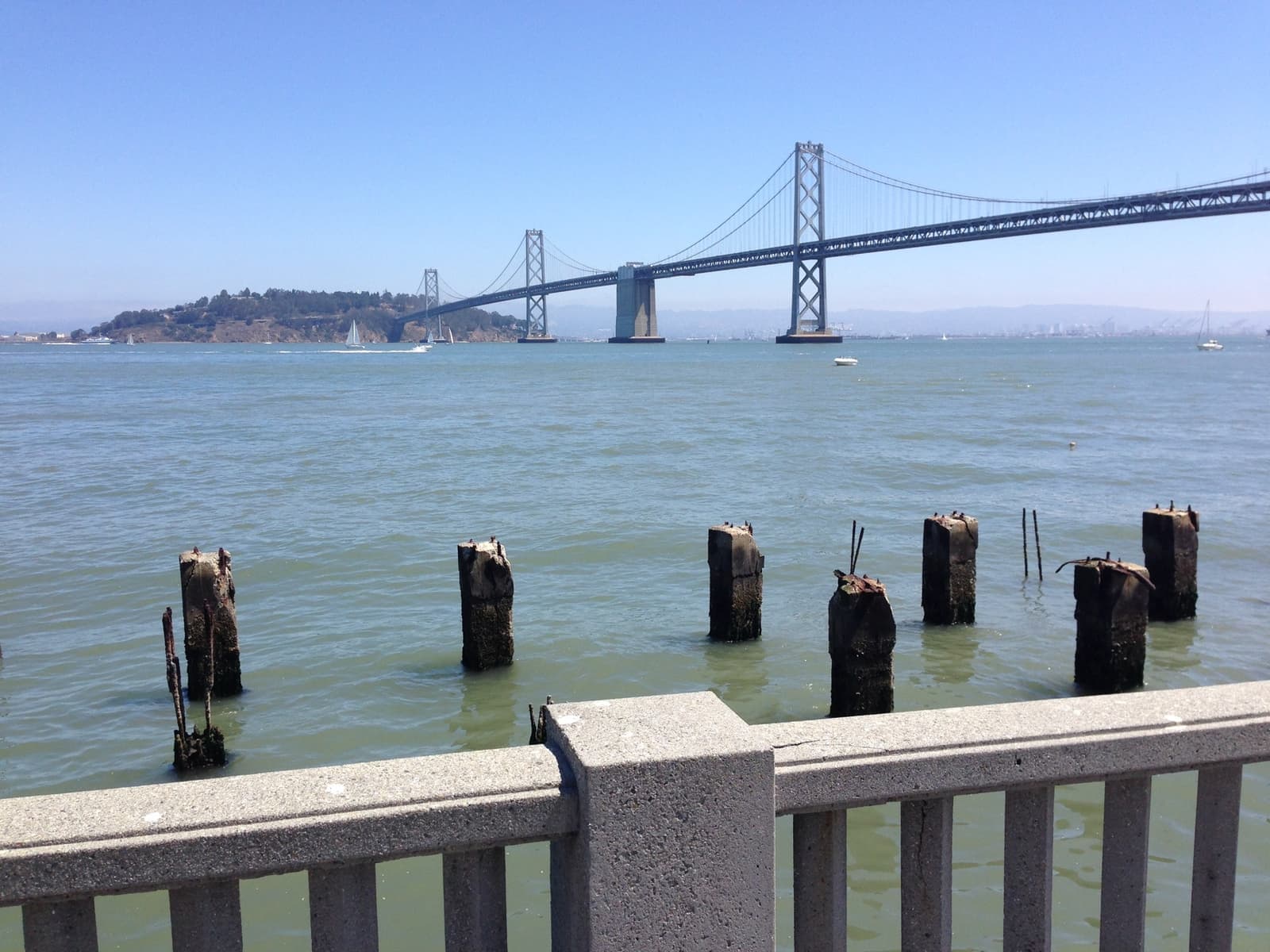 A waterfront boulevard with palm trees and the Bay Bridge beyond