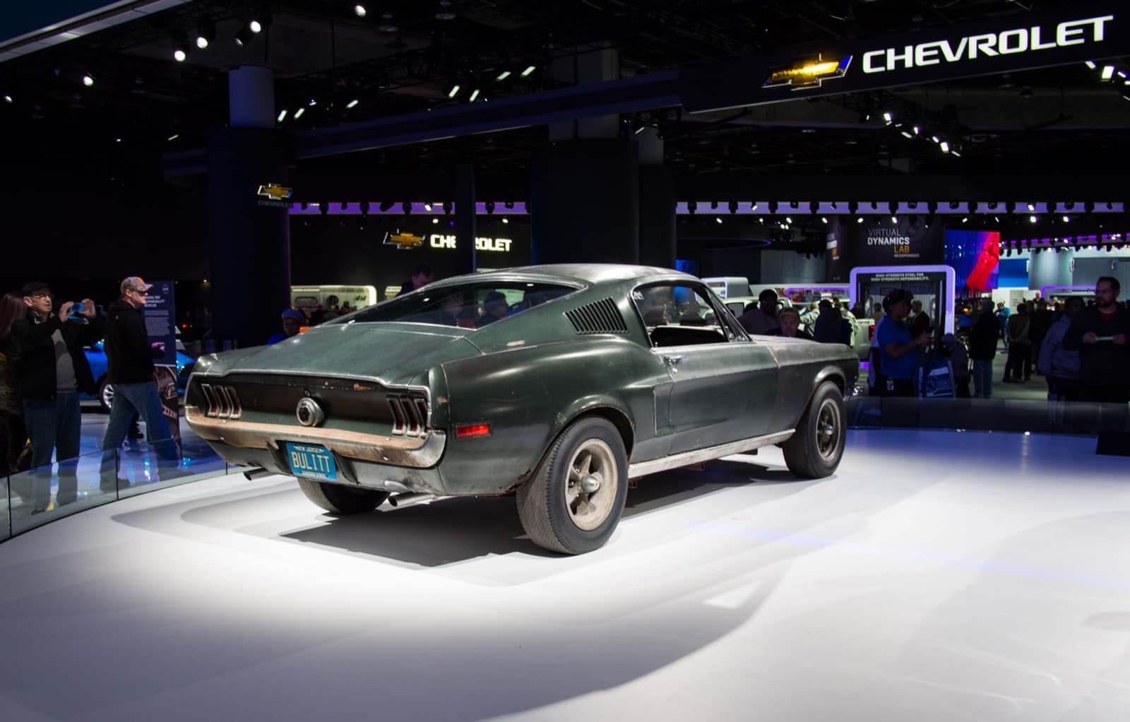 A dark green 1968 Mustang fastback with worn paint on a show stand