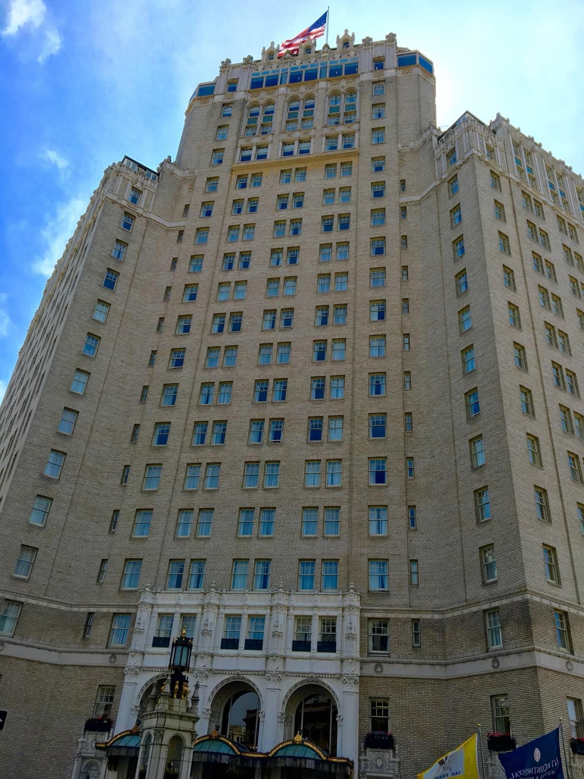 A tall cream hotel with a central tower and flags over its entrance