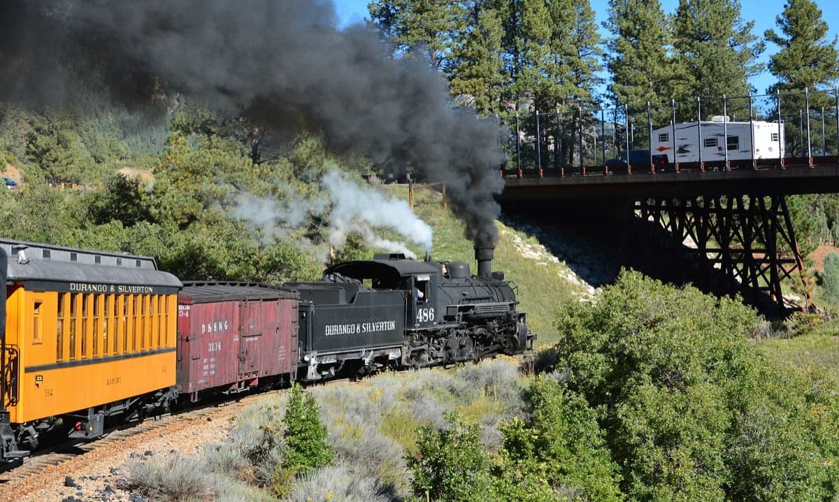 A steam train of the Durango and Silverton Narrow Gauge Railroad with a plume of smoke.