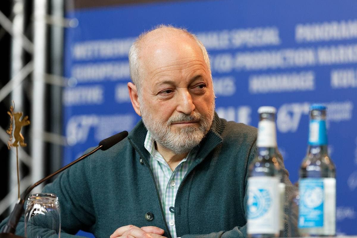 André Aciman at a press-conference table with a microphone and water bottles
