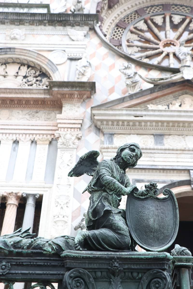 A bronze angel holding a shield in front of a carved marble porch and rose window