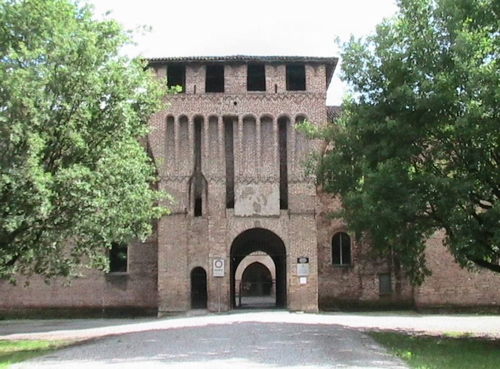 A square brick castle front with a tall arched gateway, framed by trees