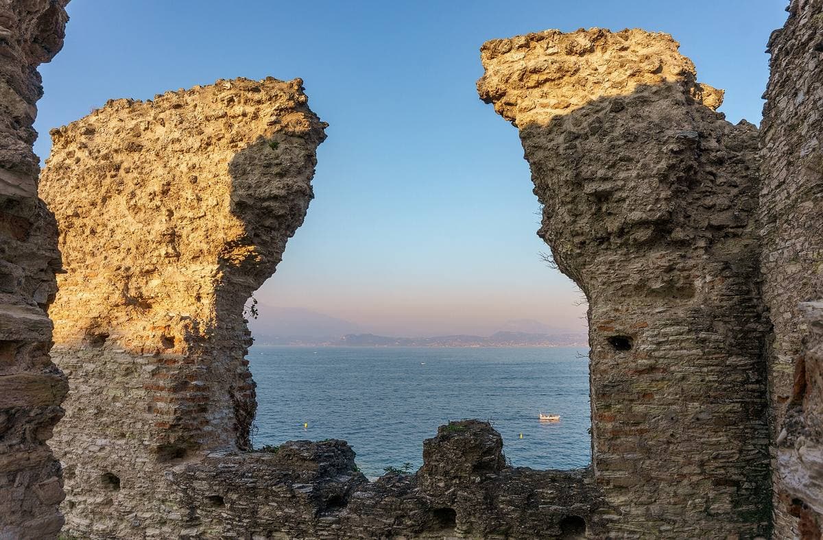 Two ruined Roman walls framing the calm lake at dusk