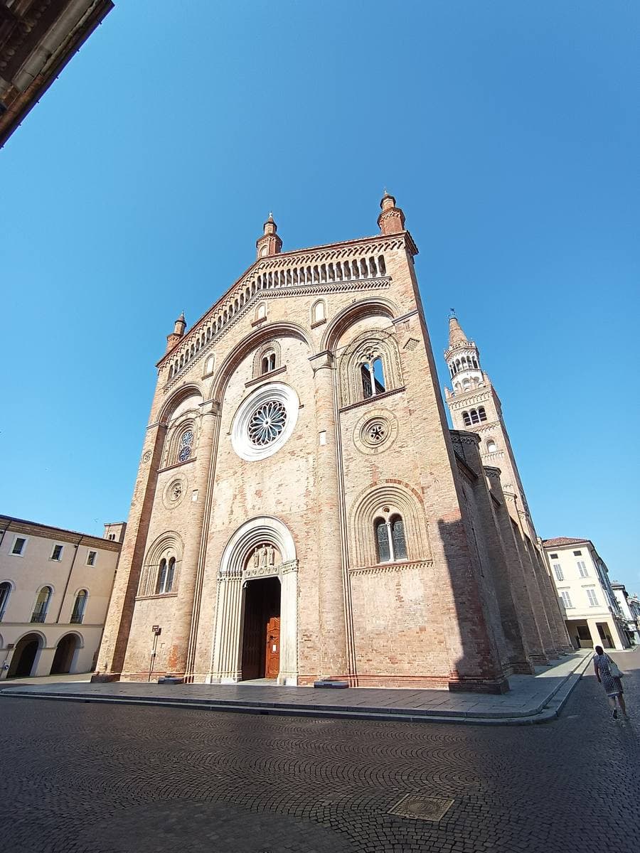 The brick and marble front of Crema cathedral under a bright blue sky