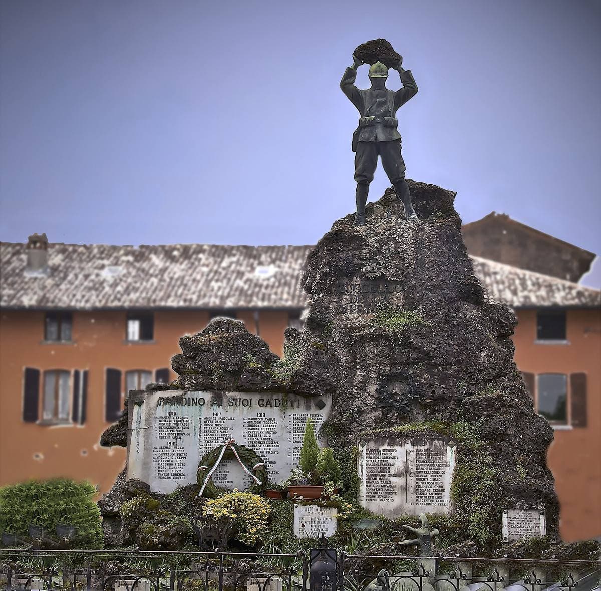 A bronze soldier holding a boulder over his head on a craggy stone base with marble name panels