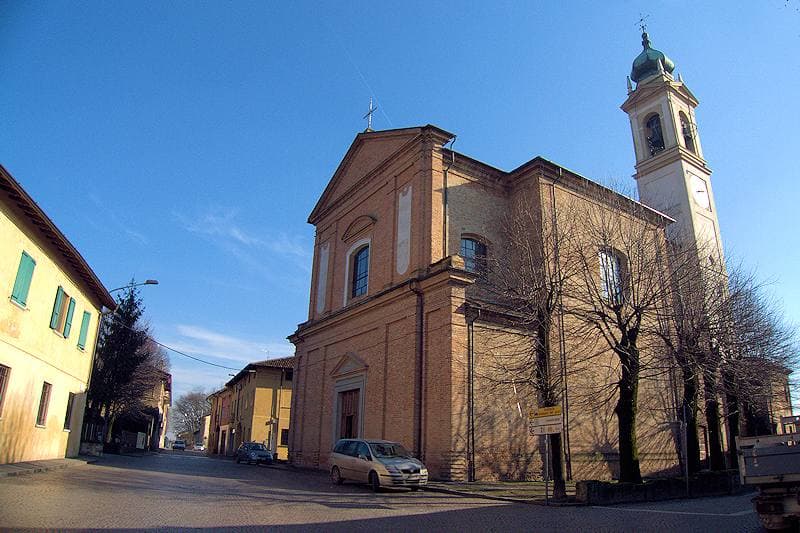 A village street with a brick church and bell tower under a blue sky
