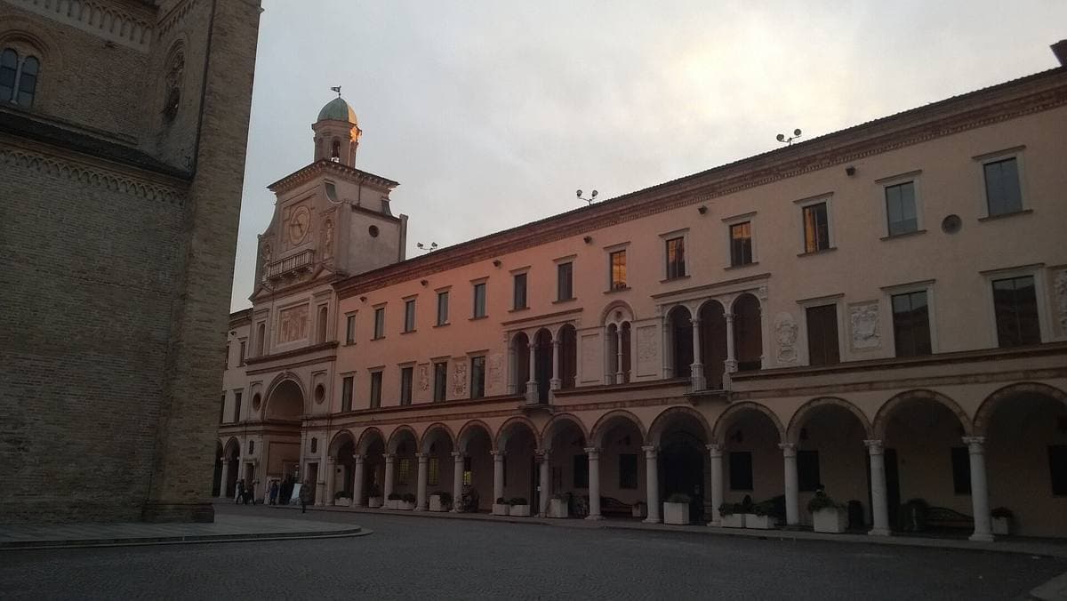 A long arcaded town hall with the Torrazzo tower at its left end, at dusk
