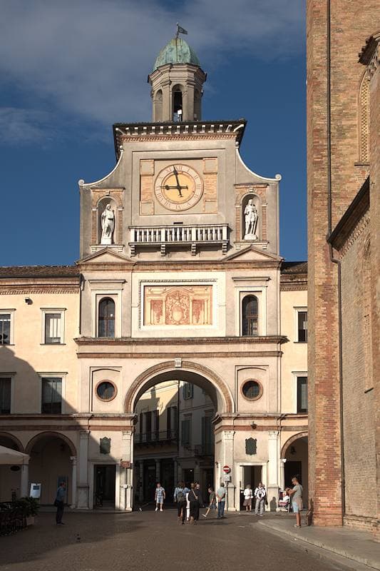 A clock-tower gateway with a deep arch, seen from the square