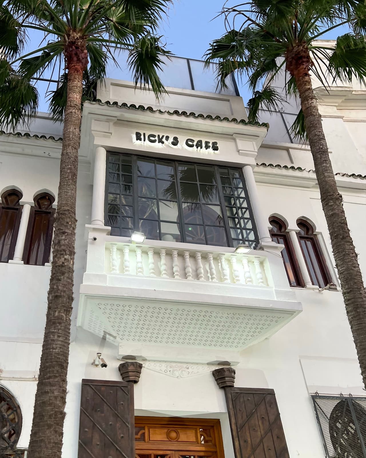 White façade of Rick’s Café in Casablanca, its name above an arched window, palms either side, blue sky