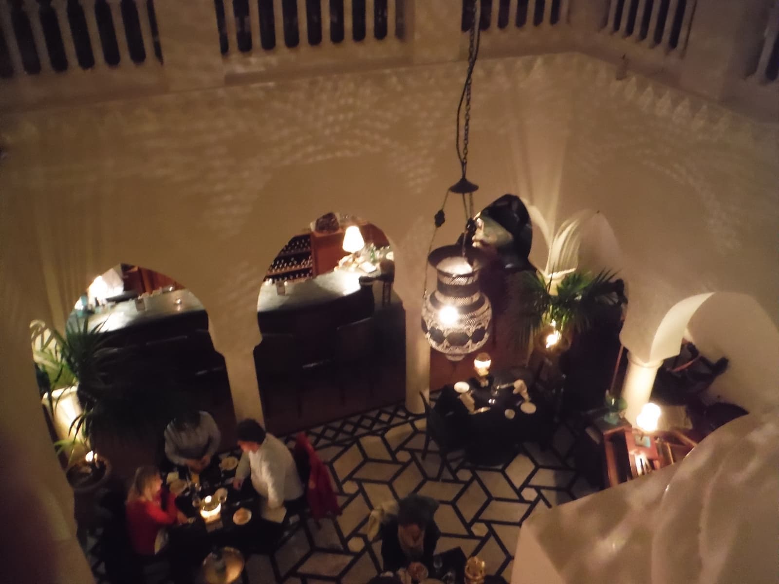 Looking down into the lamp-lit courtyard of Rick’s Café: horseshoe arches, a patterned floor, diners at small tables