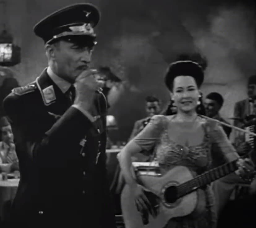 Conrad Veidt in a German officer’s cap beside Corinna Mura holding a guitar