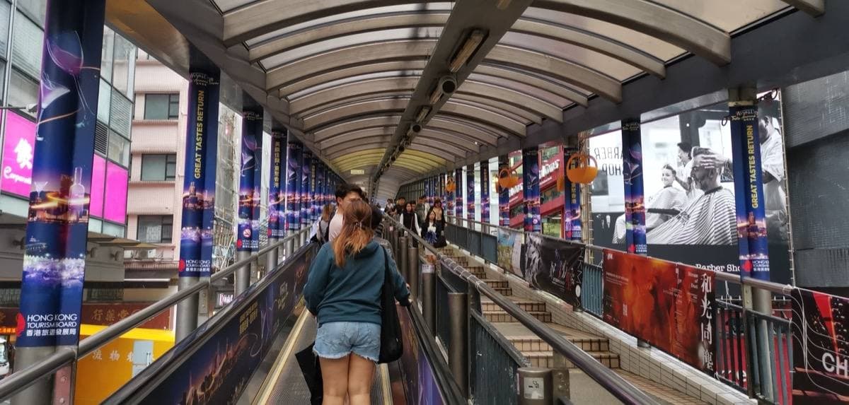 A covered escalator climbing between tall buildings above a street