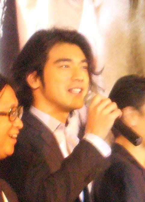 Takeshi Kaneshiro smiling, in a dark suit