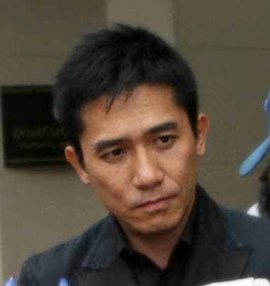 Tony Leung in a dark jacket, looking down