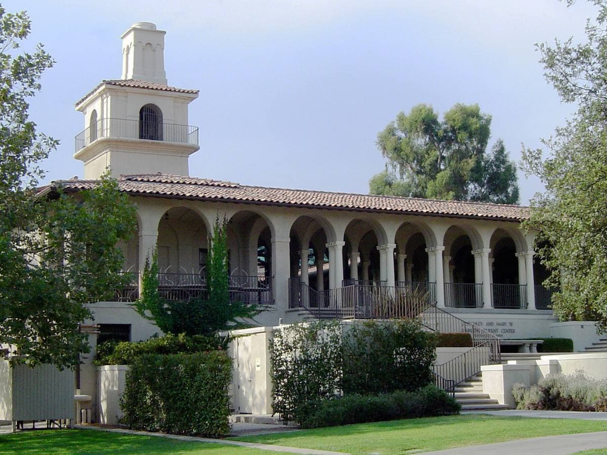 A white Spanish-style building with arches and a bell tower behind a lawn