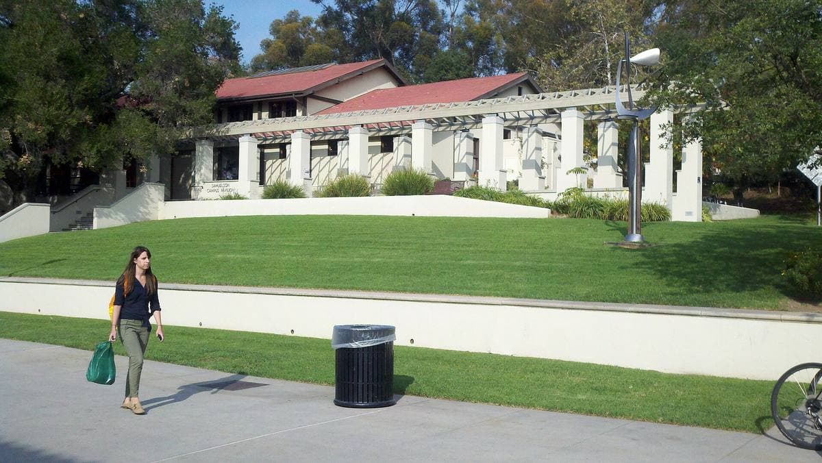A low white pavilion with a red tiled roof above a grass slope