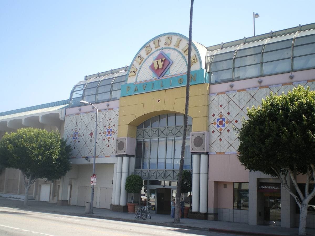 A pastel postmodern mall entrance with a glass arch and a large W