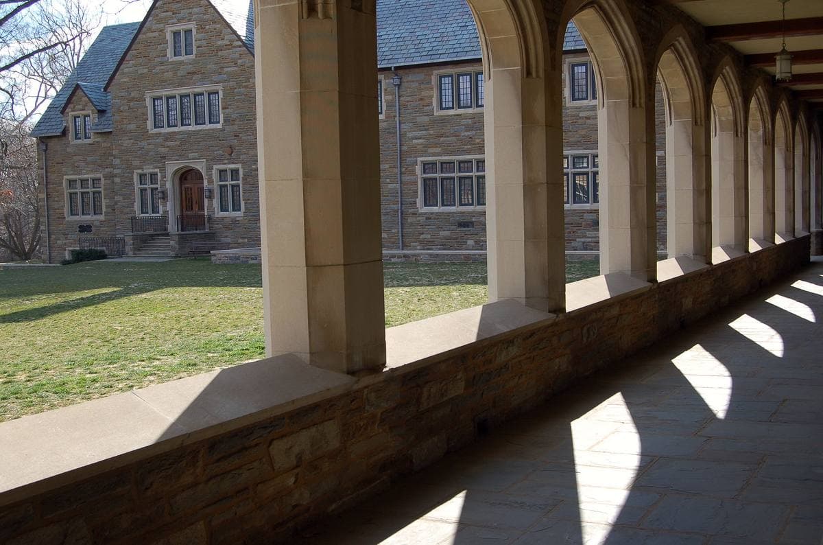A stone cloister arcade with pointed arches throwing long shadows on the flagstones