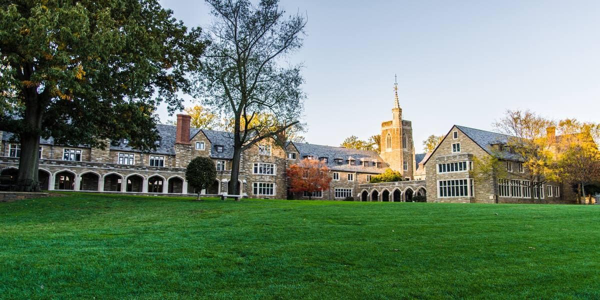 A long Collegiate Gothic school range with a tower, behind a wide green lawn in evening light