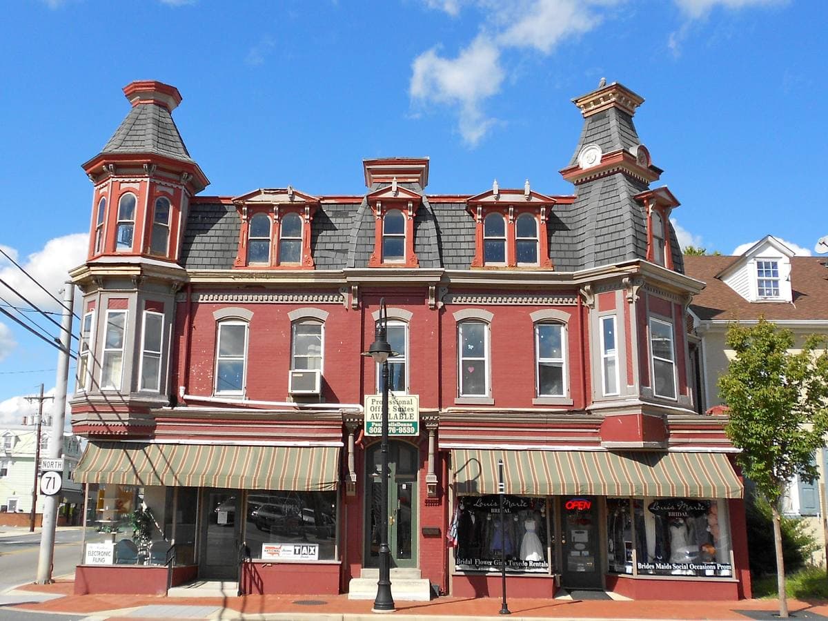 A red Victorian corner building with mansard roofs and two small towers