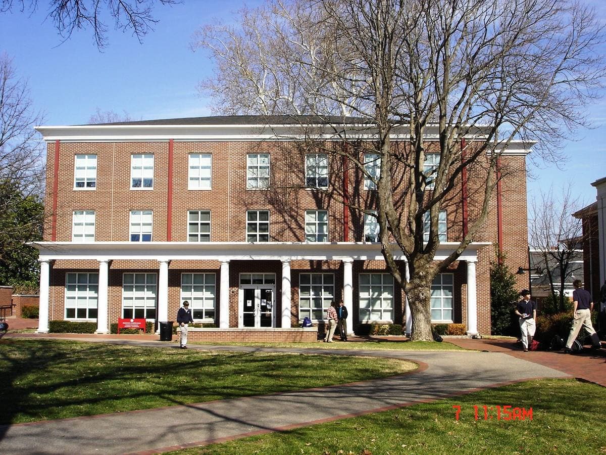 A three-storey brick school building with a white colonnade, under bare trees