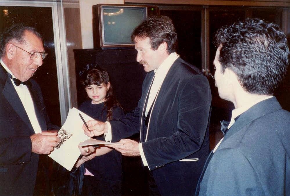 Robin Williams signing a programme for a man in a dinner jacket, a girl beside them