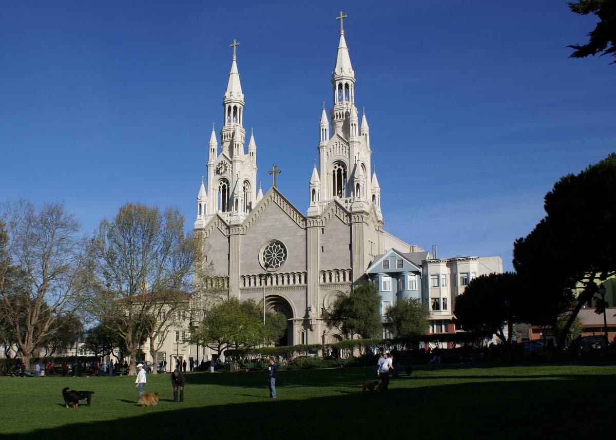 A lawn with people and a white church with two tall spires behind it