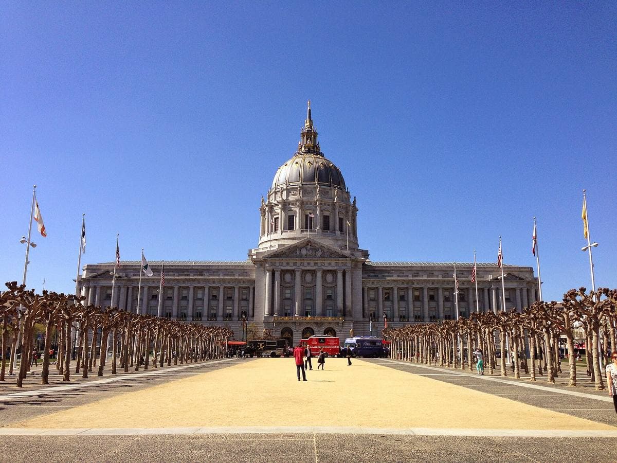 A domed Beaux-Arts city hall at the end of a plaza lined with clipped trees
