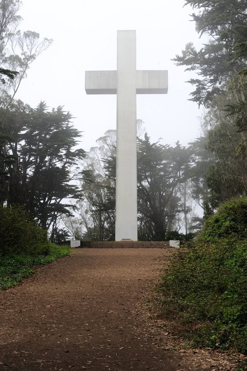 A white cross at the end of an earth path, fading into grey fog