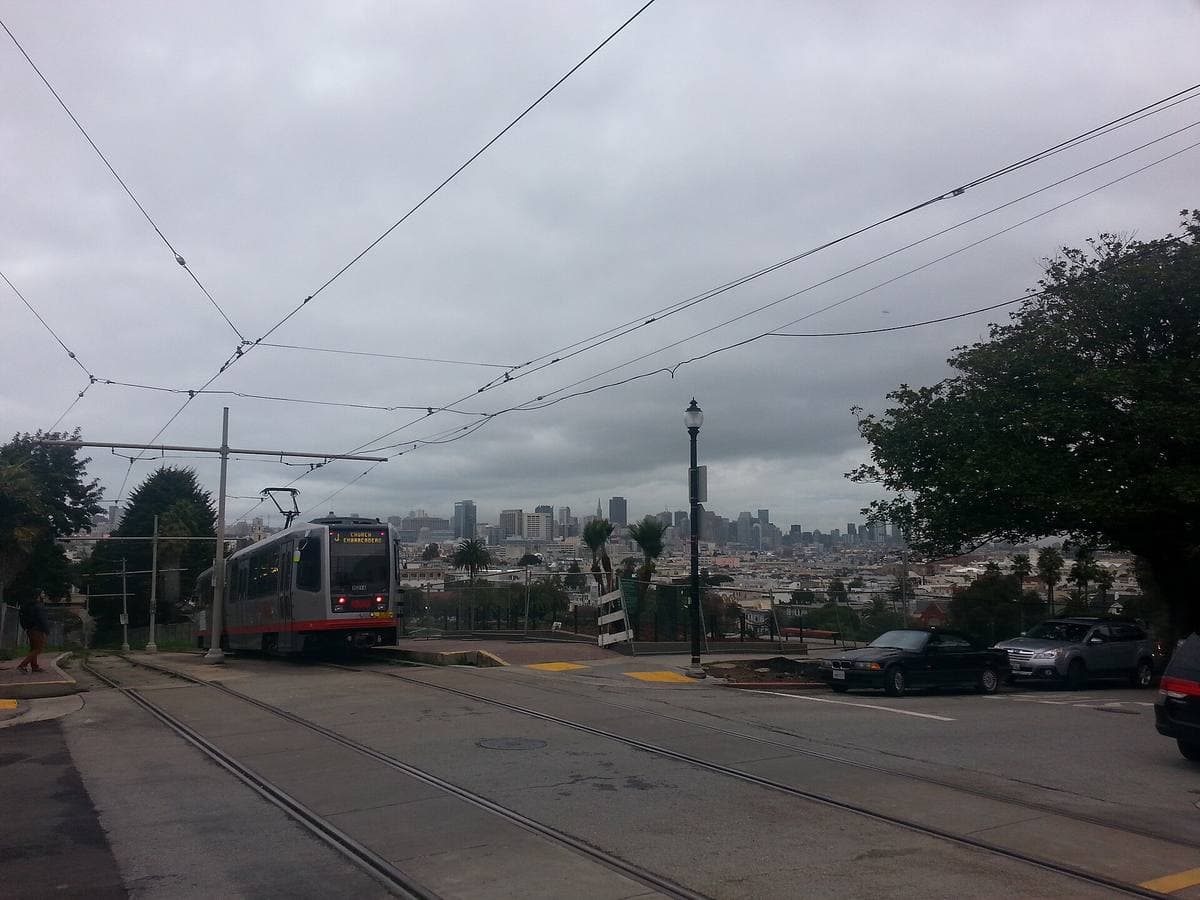 A streetcar on a grassy right of way crossing a street, the city skyline beyond
